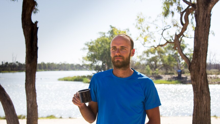 Daniel O'Callaghan holding a mug as he stands at the Lock 5 sandbar during a break from rowing.