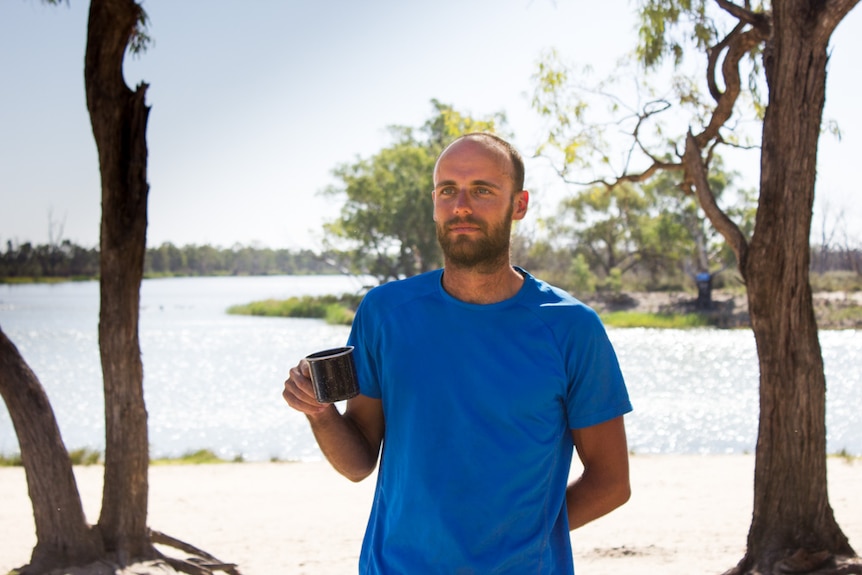 Daniel O'Callaghan holding a mug as he stands at the Lock 5 sandbar during a break from rowing.