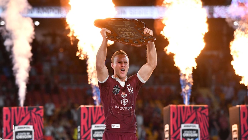 Daly Cherry-Evans holds up the State of Origin shield as columns of fire explode behind him.
