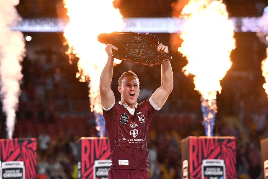 Daly Cherry-Evans holds up the State of Origin shield as columns of fire explode behind him.