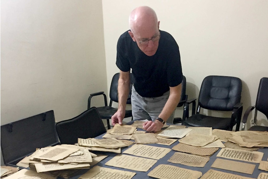 Columba Stewart examines ancient documents spread on a table