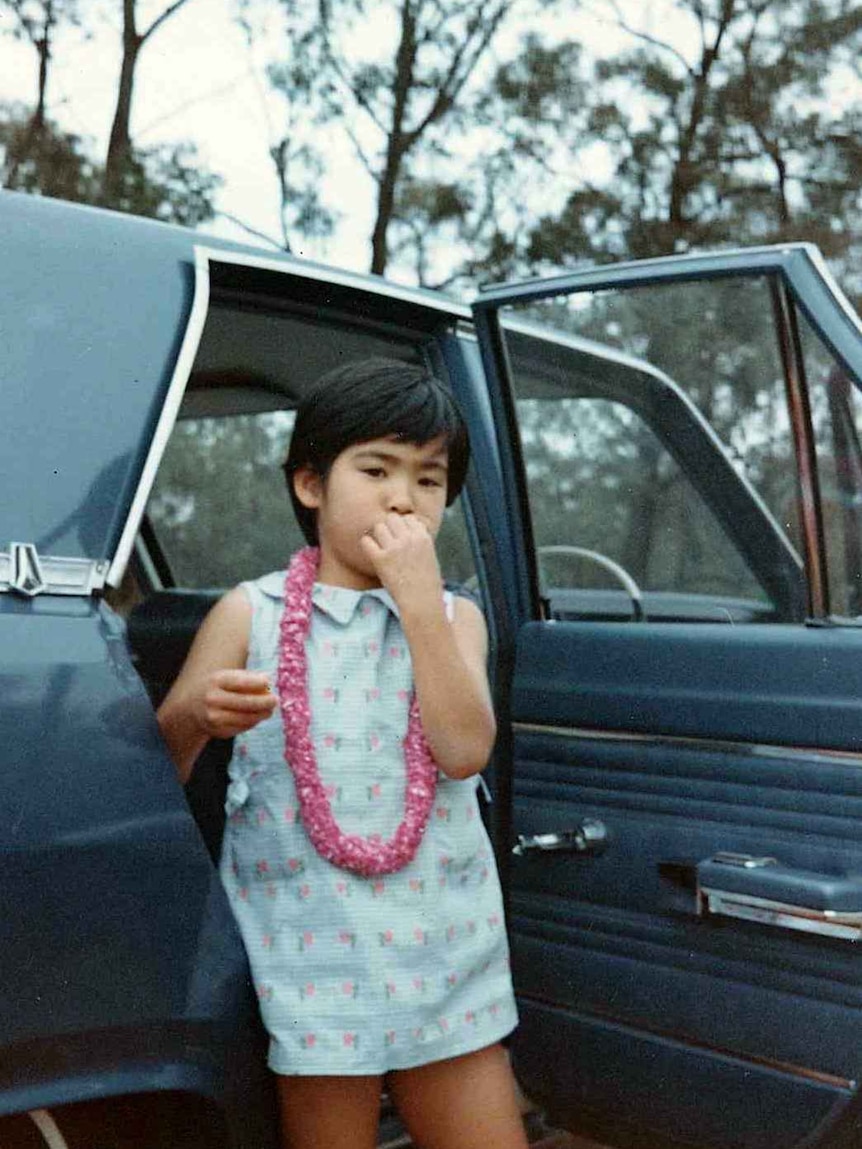 Masako stands by a car, eating.