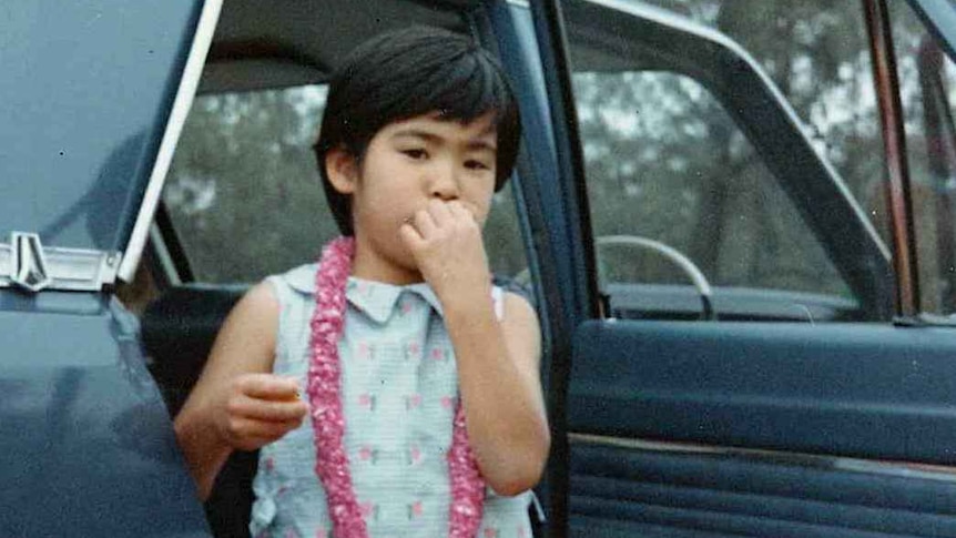 Masako stands by a car, eating.