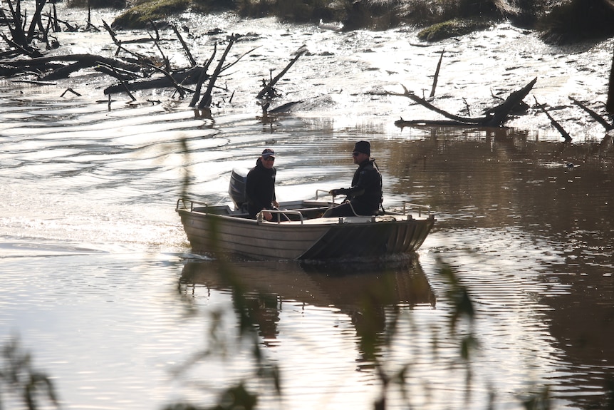 Two male police officers on a small tin boat motor down a muddy river.