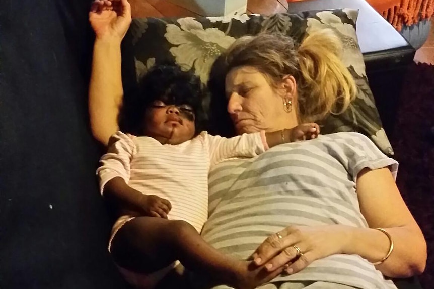 A woman and a small child asleep on a black couch.