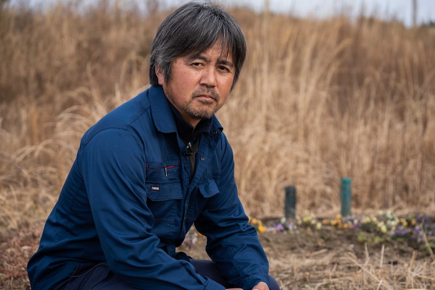 A Japanese man with salt and pepper hair crouching in a field