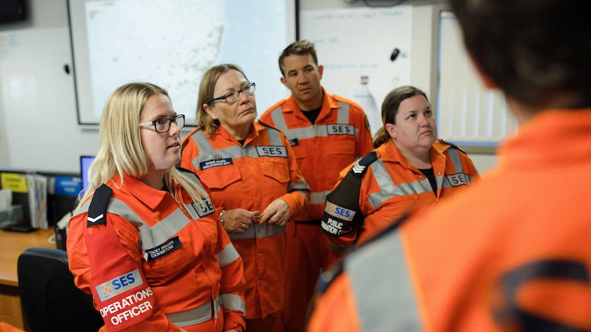 People in uniforms of orange overalls stand listening to instructions during a state emergency in NSW
