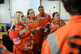 People in uniforms of orange overalls stand listening to instructions during a state emergency in NSW
