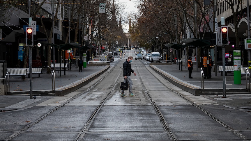 A person wearing a face mask crosses a quiet Bourke Street Mall in Melbourne.