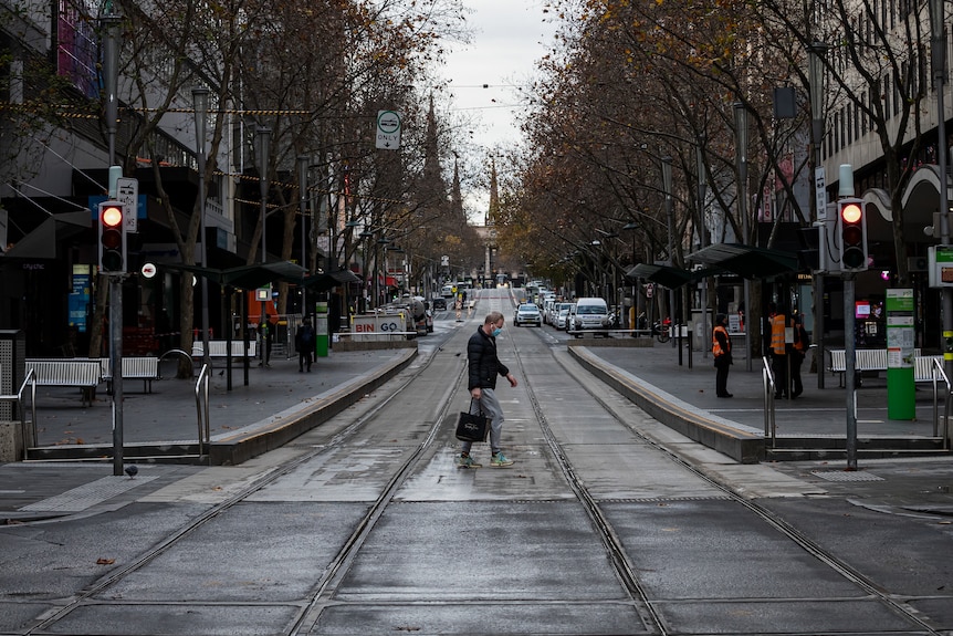 A person wearing a face mask crosses a quiet Bourke Street Mall in Melbourne.