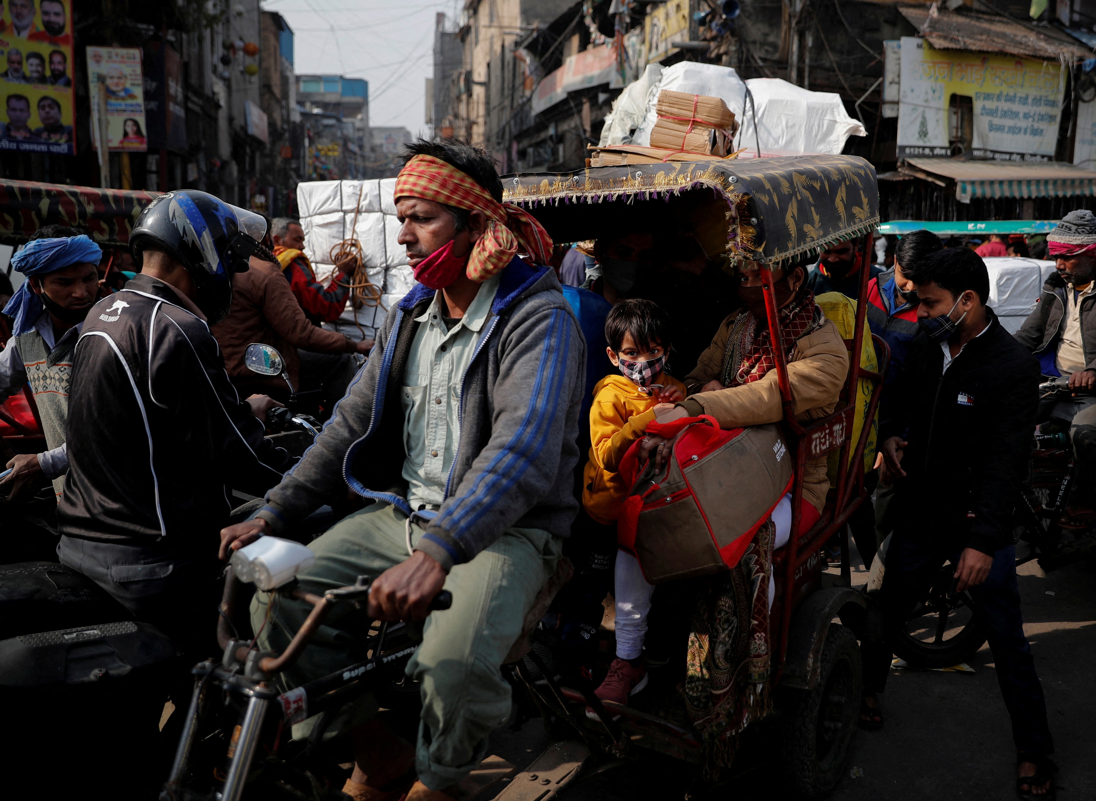 A man cycles a bike while carrying a family on a rickshaw in a crowded market