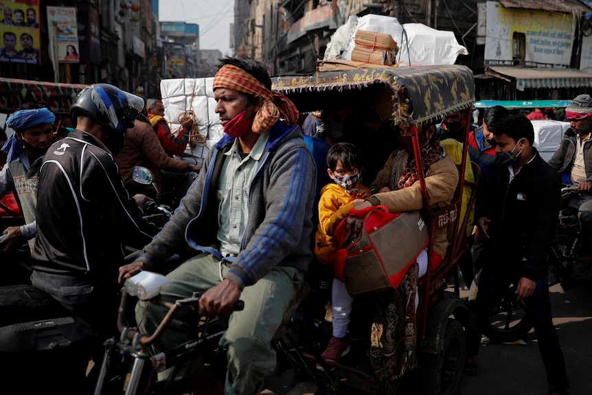 A man cycles a bike while carrying a family on a rickshaw in a crowded market
