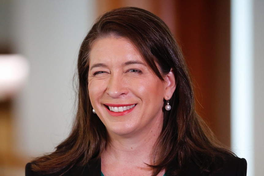 A woman with shoulder length brown hair smiling, wearing a green shirt and black blazer