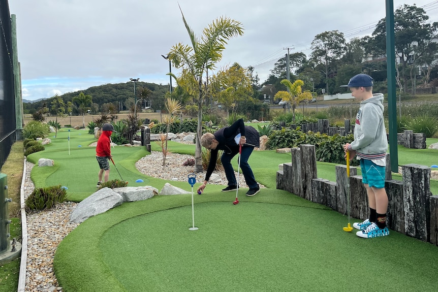Two grandsons under five playing mini golf with their Grandma. 