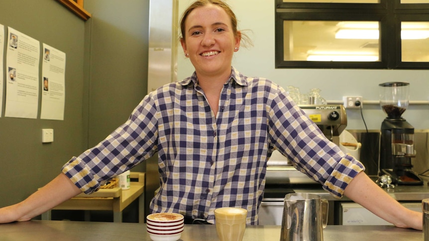 Beth Ostini stands behind two coffees on a bench in a TAFE training room