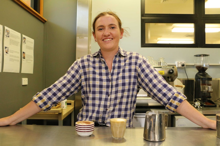 Beth Ostini stands behind two coffees on a bench in a TAFE training room
