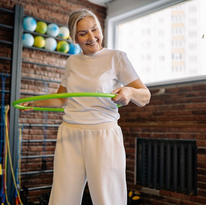A woman in a gym using a hula hoop.