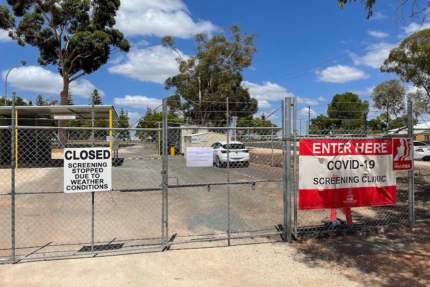 A metal gate blocks an outdoor COVID-19 testing site, with a sign explaining it is closed due to the weather conditions.
