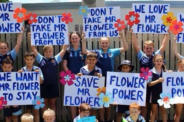 A group of school students stand together holding signs that read Don't take Mr Flower from us.