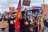 People march the streets holding placards and Aboriginal flags.