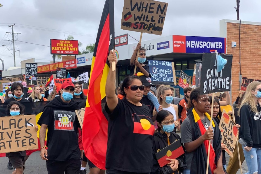 People march the streets holding placards and Aboriginal flags.