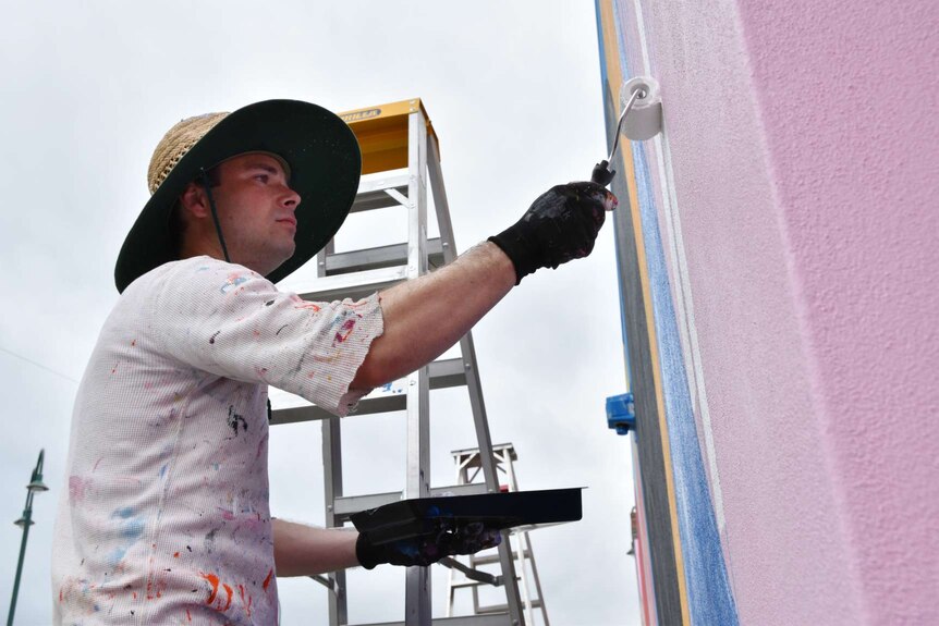 US artist Hense holds a paint roller and tray as he paints a wall at the top of York Street in Albany.