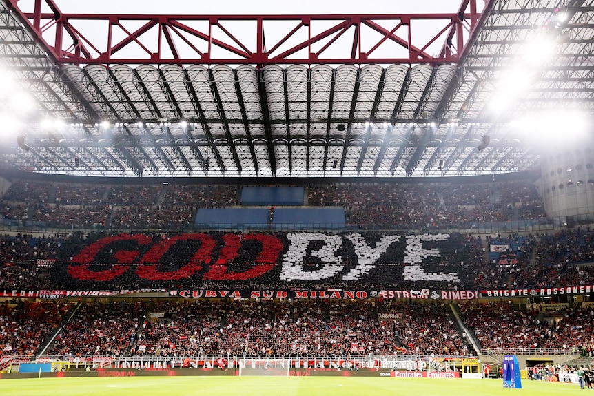 Football fans in a section of a stadium grandstand hold cards forming a sign saying 'Godbye'.