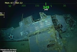 A decaying aircraft lies at the bottom of the ocean. It is covered in barnacles.