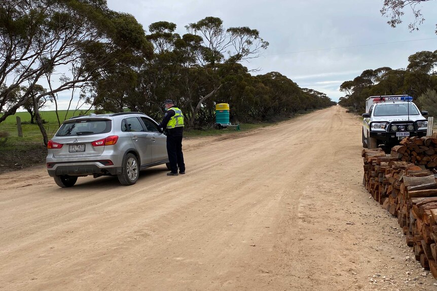 A police officer talks to a driver on a dirt road border crossing