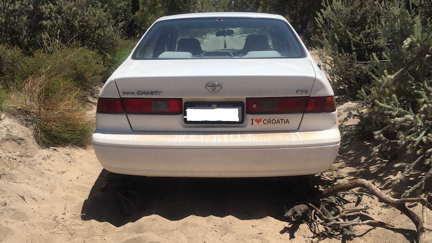 The rear of a white Toyota Camry parked on sand in bushland, with an 'I love Croatia' bumper sticker.