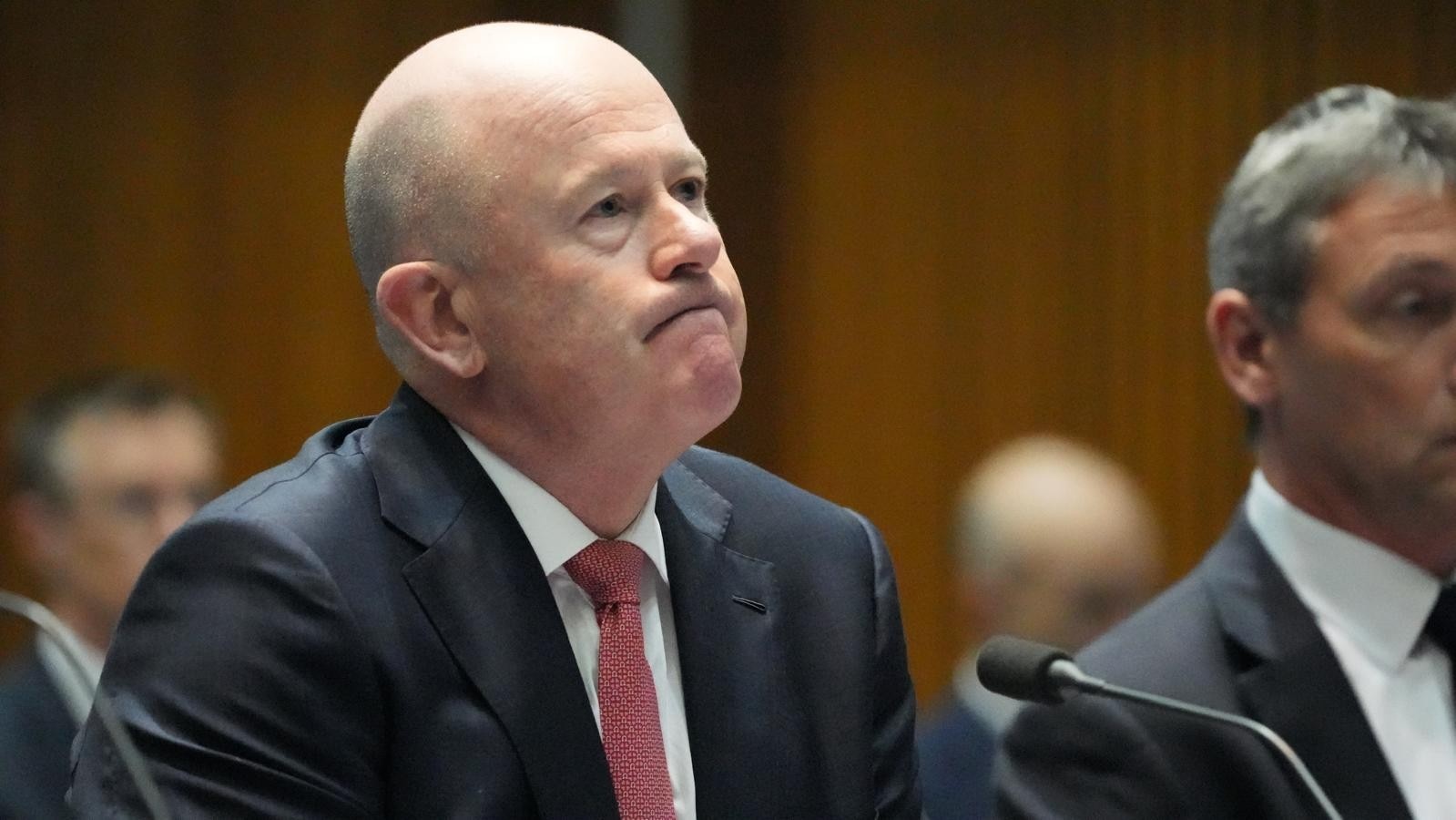 A bald man in a suit and tie purses his lips.