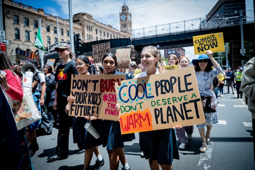 School girls carry signs including 'Cool People don't deserve a warm planet', students march behind them.