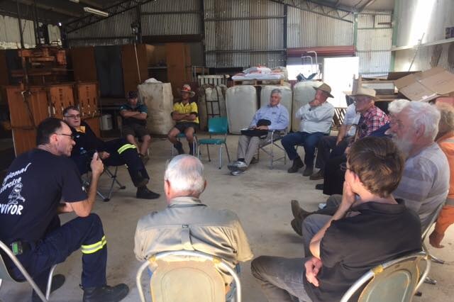 A group of elderly men sit in a circle in a shed.