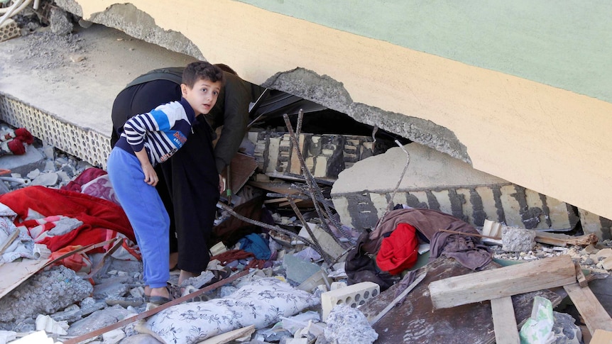 A man and a boy look at a damaged building from an earthquake.