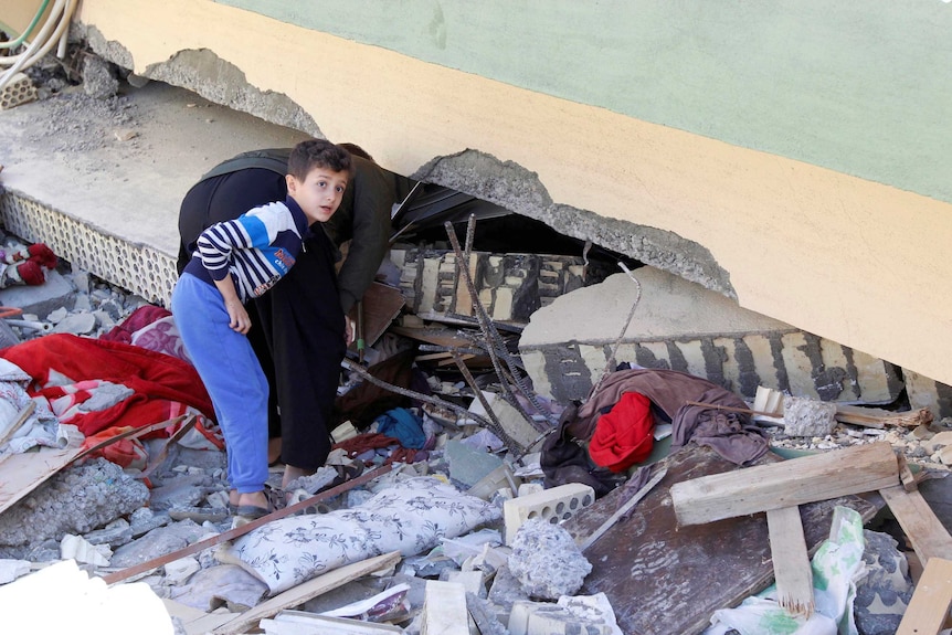 A man and a boy look at a damaged building from an earthquake.