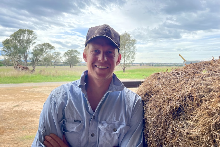 A man smiling while leaning on a hay bale