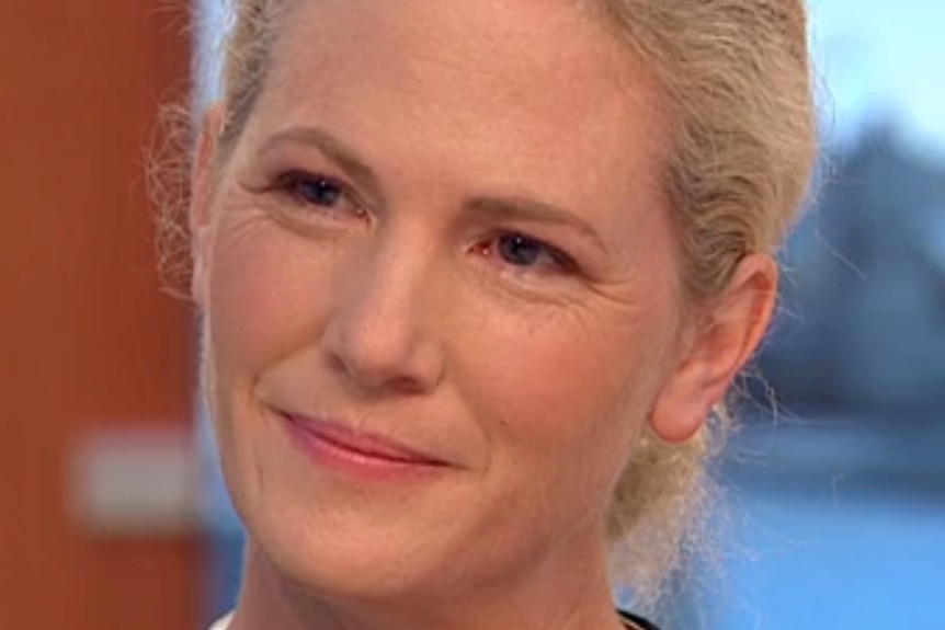 Tight headshot of woman with fair skin and blond hair slightly smiles looking to the left of camera. 