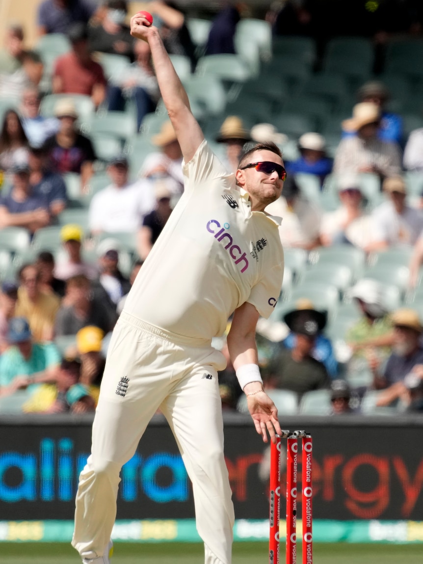 A man in cricket whites and sunglasses is photographed in the middle of his bowling action