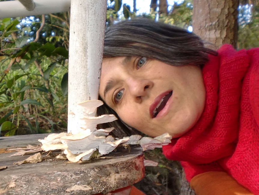 Woman leaning sideways looking at the foot of a white plastic chair where fungi is growing and decomposing the chair.