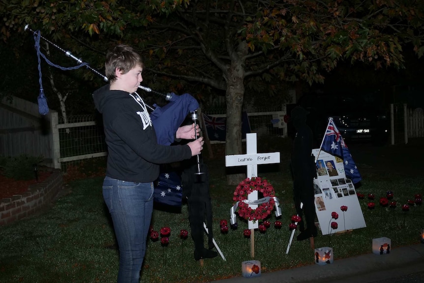 A teenage boy plays the bagpipes near Anzac Day commemorative items