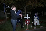 A teenage boy plays the bagpipes near Anzac Day commemorative items