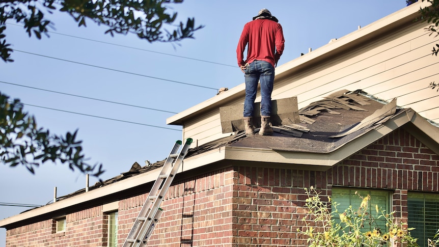 A man inspecting roofing works on top of a house