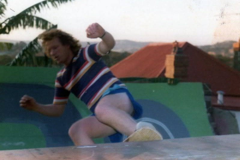 Bob Hastie skating up a ramp, wearing a striped t-shirt.