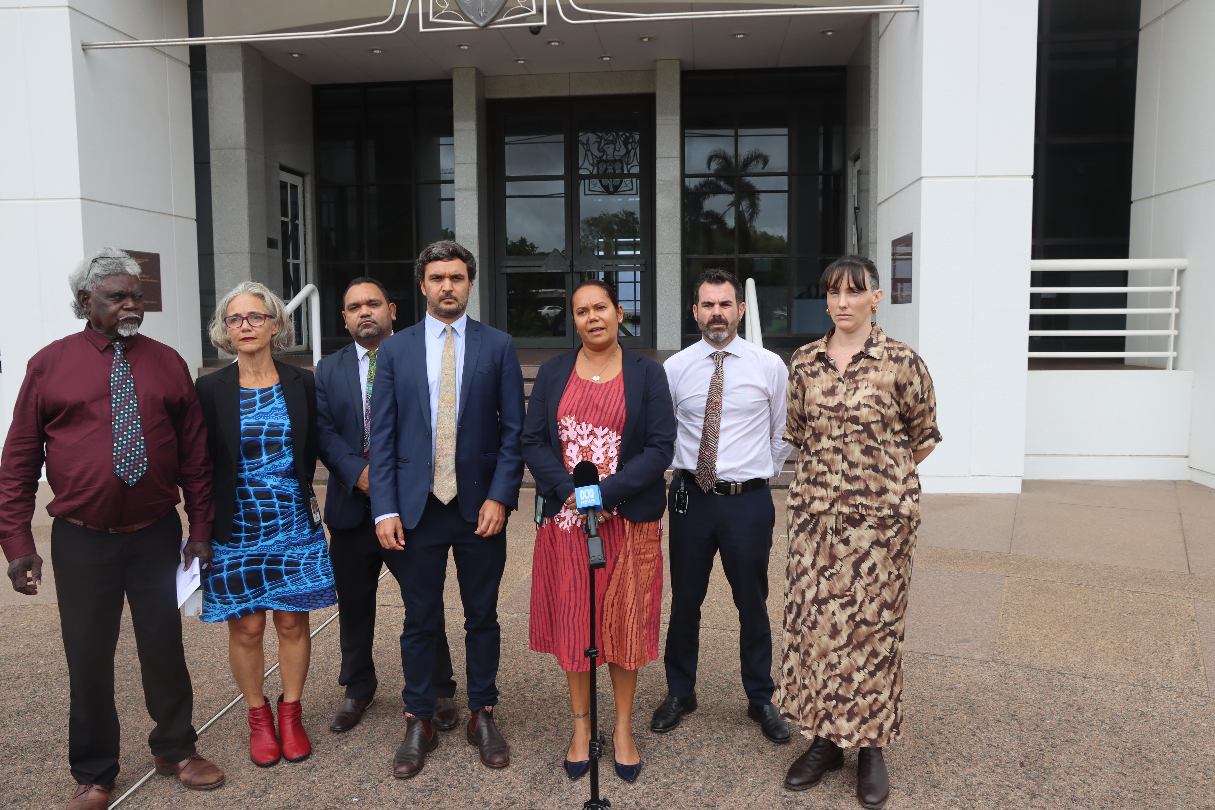 Siete personas se paran frente a un edificio blanco.