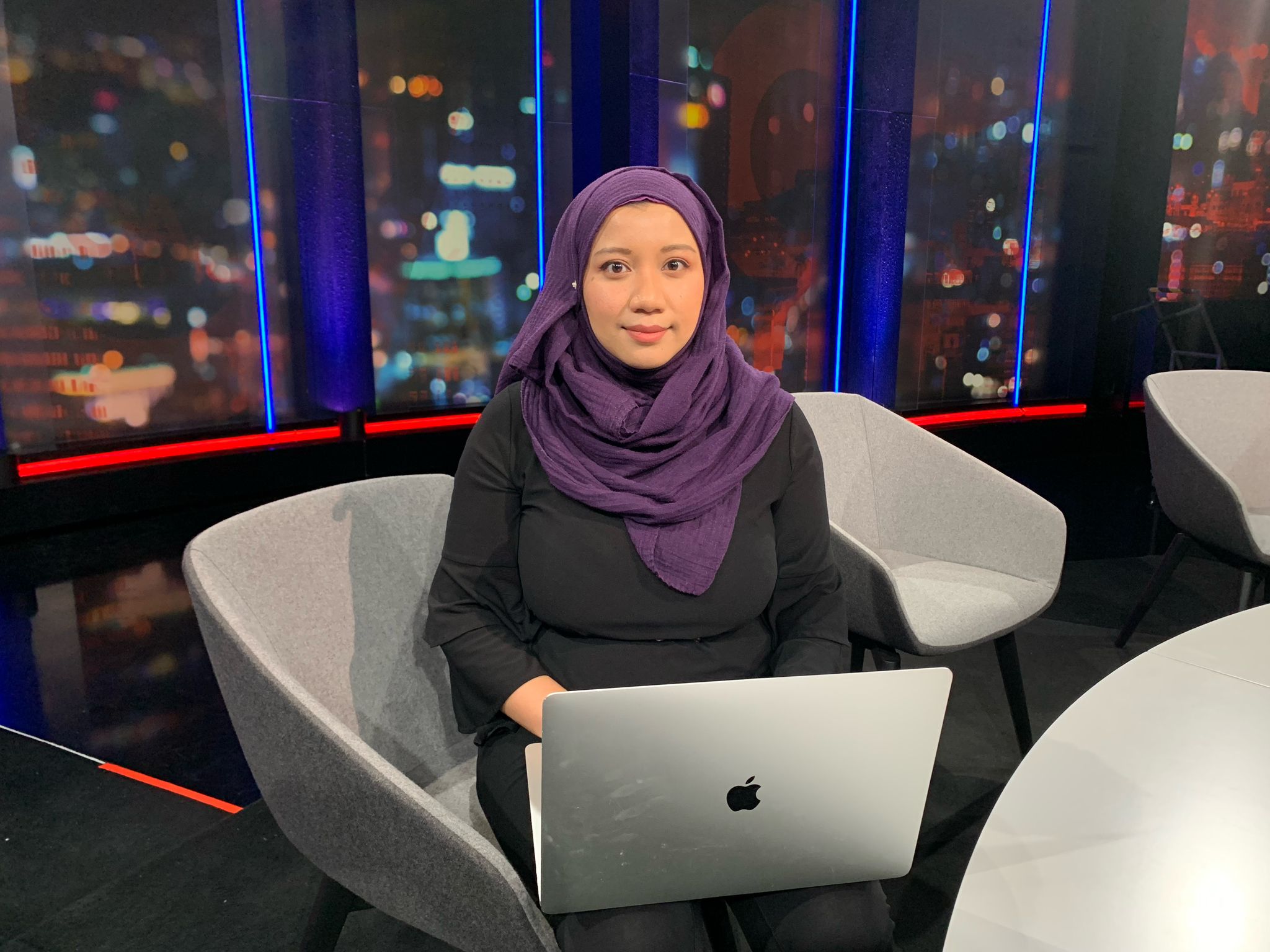 A woman in a black dress and a purple headscarf sitting with a laptop on her lap