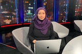A woman in a black dress and a purple headscarf sitting with a laptop on her lap