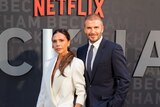 Victoria Beckham and David Beckham pose for a photo, wearing suits, in front of a Netflix media wall