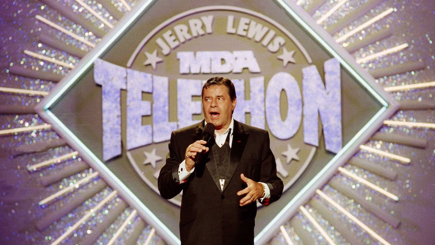 Entertainer Jerry Lewis stands on a stage speaking into a microphone.