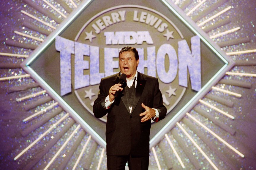 Entertainer Jerry Lewis stands on a stage speaking into a microphone.