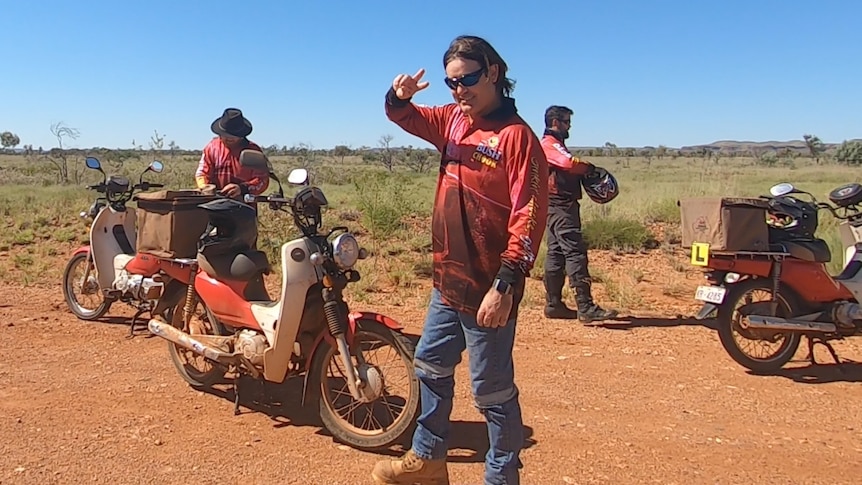Postie bike, some with L-plates, stop on a red-dirt road in the Pilbara